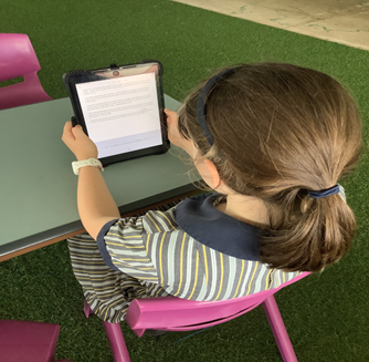 Photo of Lara sitting at her desk at school with her tablet. 