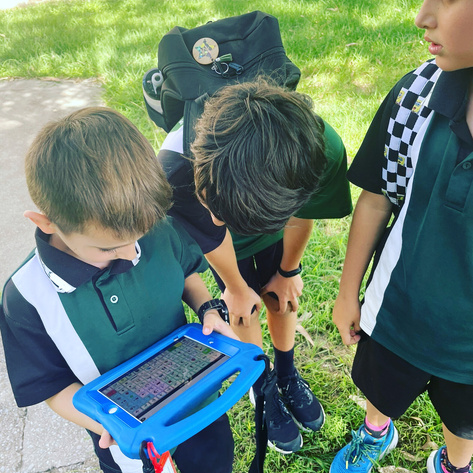 Photo of darcy and two primary school boys in uniform looking at Darcy's communication device