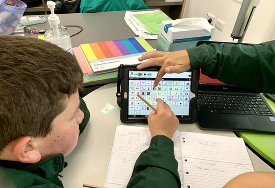 Photo of Will and his peers gathered around his AAC device