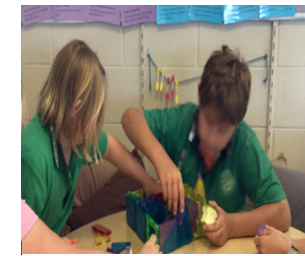 Photo of Eva at school with another student who are building something together with magnetic tiles