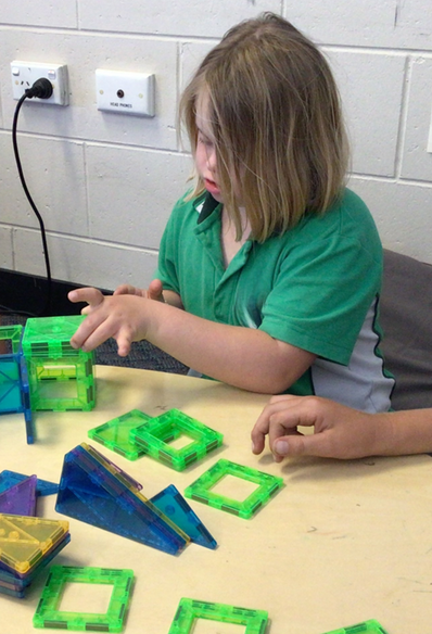 Photo of Eva in her uniform at school building a structure with magnetic tiles