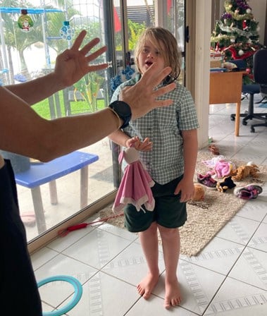 Photo of Eva at home in her uniform, an adult is holding up their fingers and Eva is counting them.