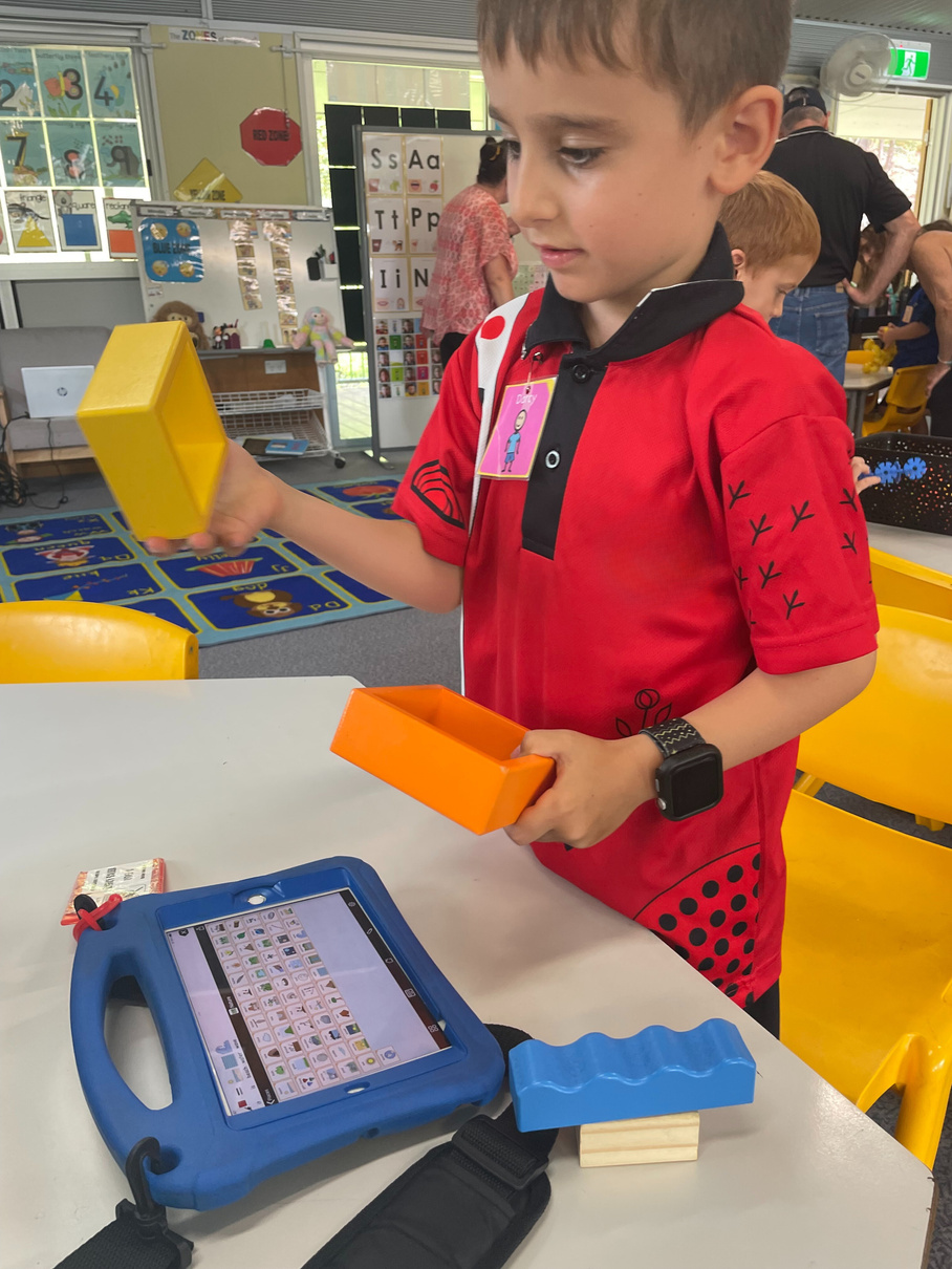 Photo of Darcy at school with large blocks and his communication device on the table