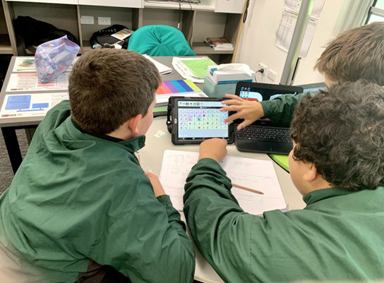 image of three highschool boys gathered around an ipad showing a vocabulary board and working on an assessment