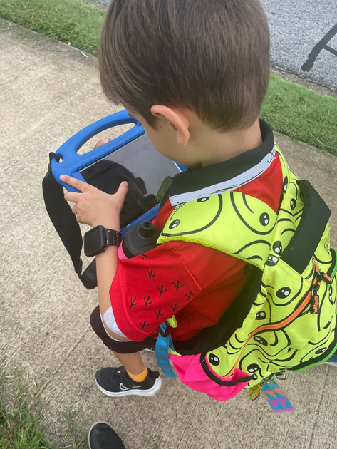 Photo of Darcy from above in his uniform and backpack using his AAC device