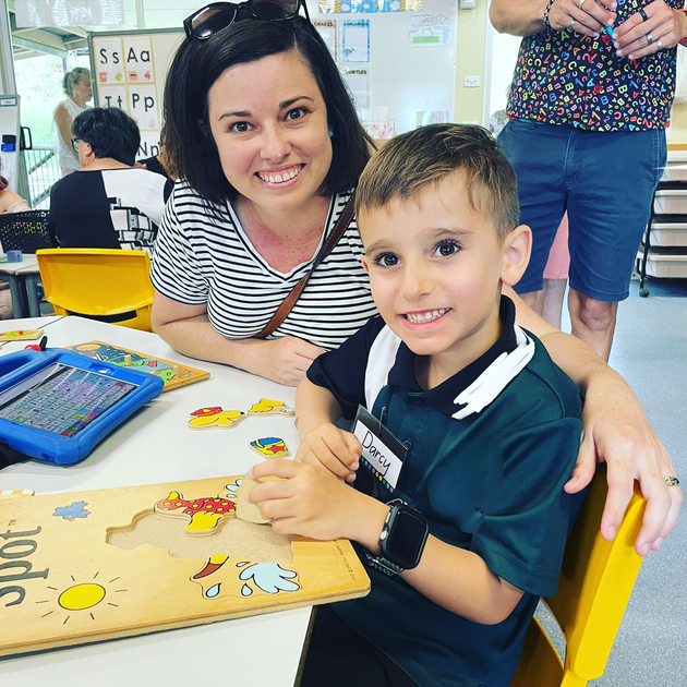 photo of Darcy and his mum at school. Darcy is sitting at the table with a puzzle.